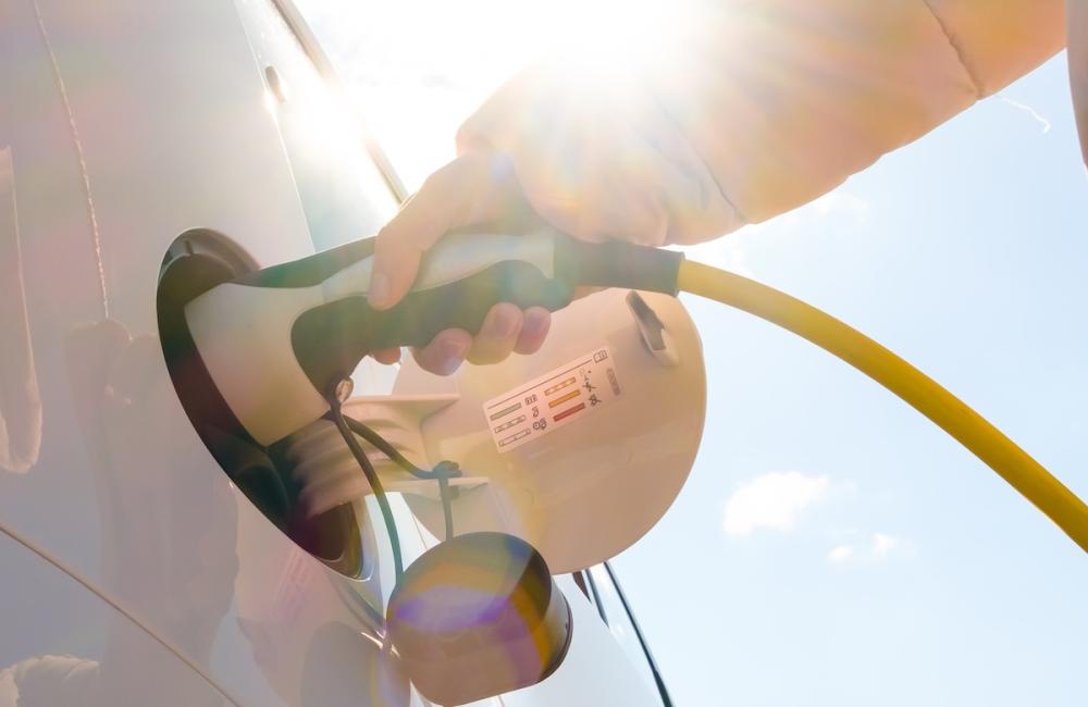 Close up woman hand inserts power cable supply to charge electric or EV car at sunlight. Image from Envato