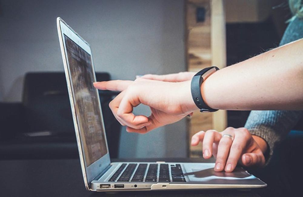 Person pointing at a laptop screen during a discussion, with a focus on collaboration and technology.