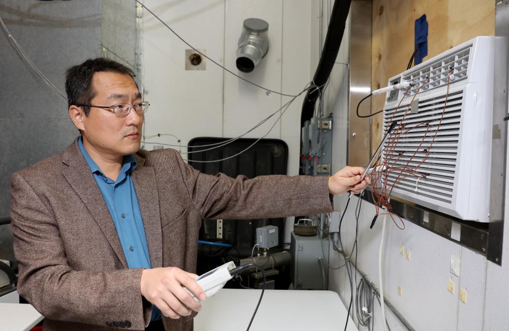 Oak Ridge National Laboratory’s Bo Shen works with a prototype window air conditioning unit that cools using propane, which lowers costs, increases efficiency and benefits the environment.