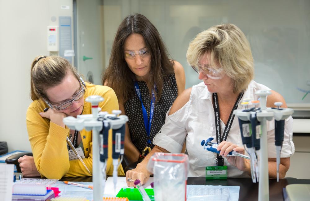 Flora Meilleur (middle) works with teachers participating in her project, helping them mix the protein solution lysozyme with a salt solution to form a crystal. The teachers mix the solutions in various concentrations and ratios and observe the results.