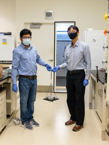 ORNL scientists Md Anisur Rahman (left) and Tomonori Saito (right) demonstrate the strength of a novel tough adhesive. A drop the size of 1 square centimeter can hold 300 pounds. Credit: Carlos Jones/ORNL; U.S. Dept. of Energy.