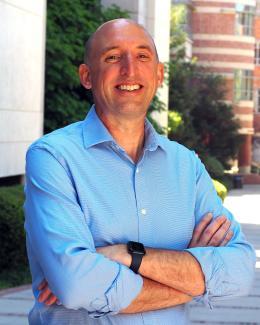 A man smiles at the camera with his arms crossed