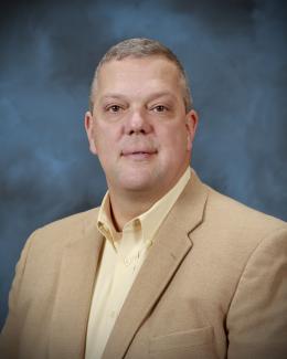Portrait of a man wearing a yellow shirt and camel colored jacket
