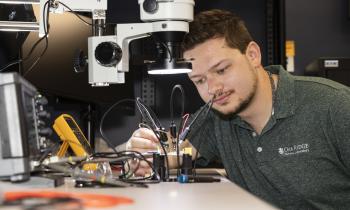 A man looks at a circuit board under a microscope.