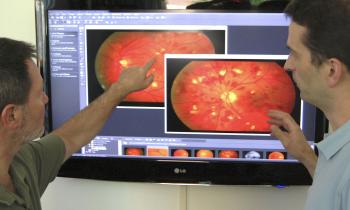 two researchers discuss a close up scan of a retina on a computer monitor