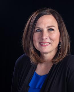 Headshot of a middle aged female with shoulder length, brown hair, wearing a blue and black top.  