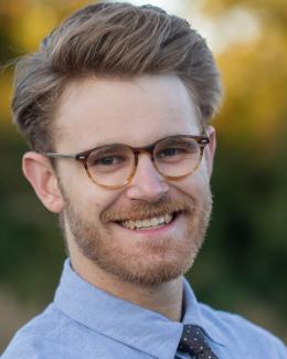 Headshot of Connor J. Parker. Glasses tie shirt beard.
