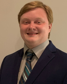 Photo of smiling man with blonde hair, wearing a blue striped tie, gray dress shirt and blue suit jacket