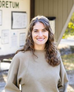 Outside portrait of KC with shoulder-length brown hair wearing a light green sweatshirt.