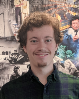 Young man with a mustache and flannel shirt in front of ORNL History Painting