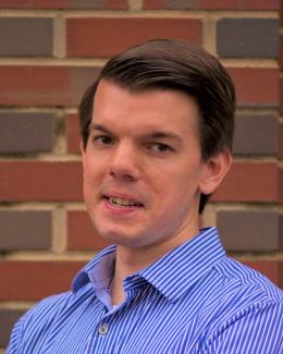A portrait headshot with a red brick wall background