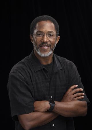 a smiling person in a black button up shirt in front of a dark background