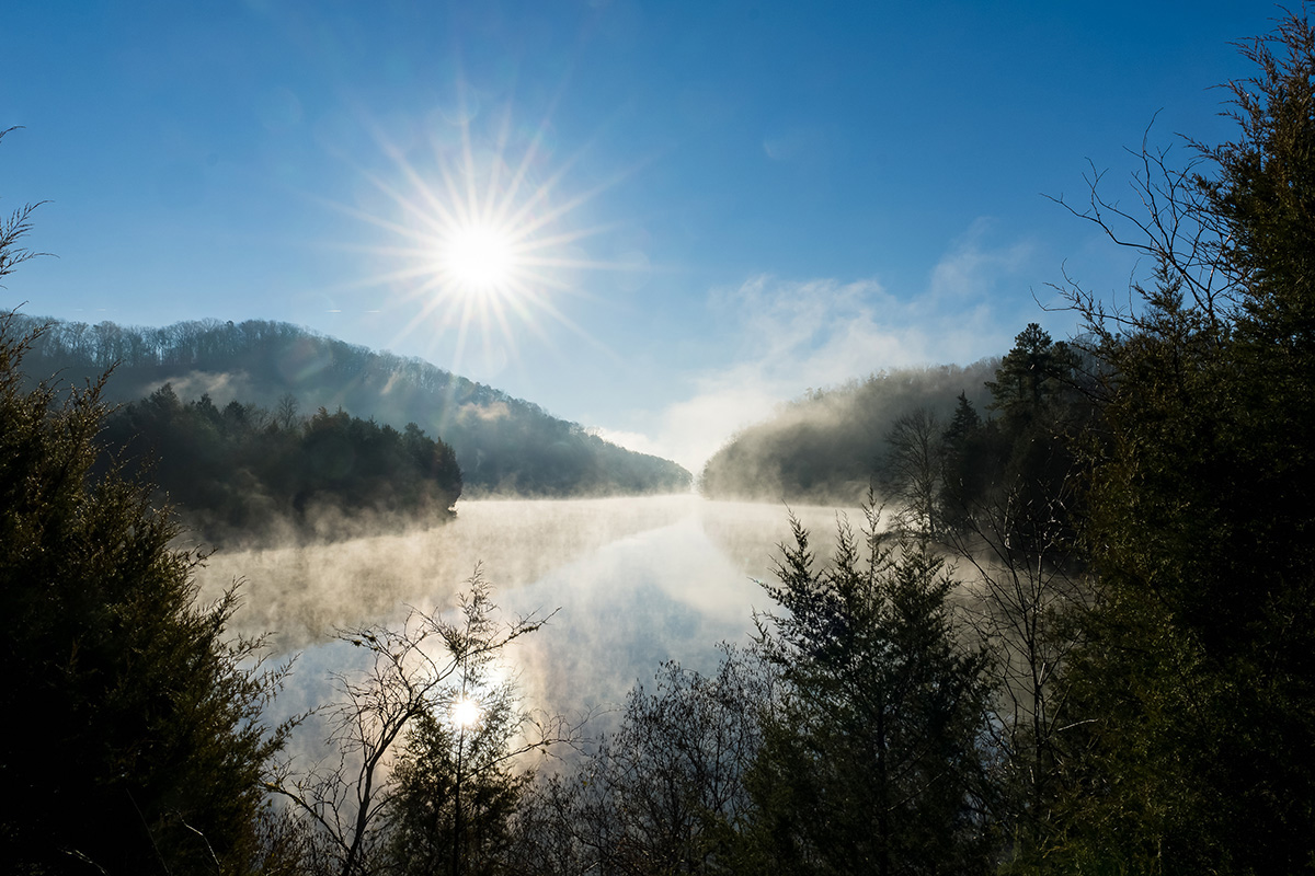 Landscape image of lake near ORNL with the sun beaming down and fog spread across the water