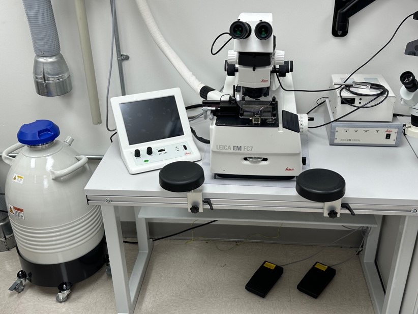 a complex modern microscope next to a small monitor on a tabletop, with a canister on the floor
