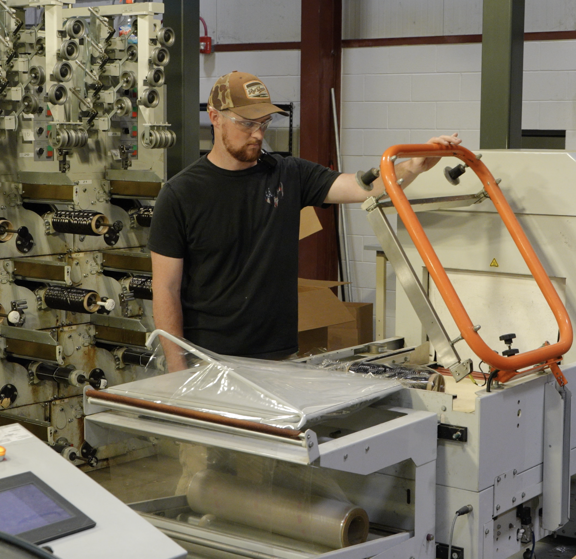 Technician operates packaging equipment, guiding a sheet of material through a sealing machine in an industrial lab.