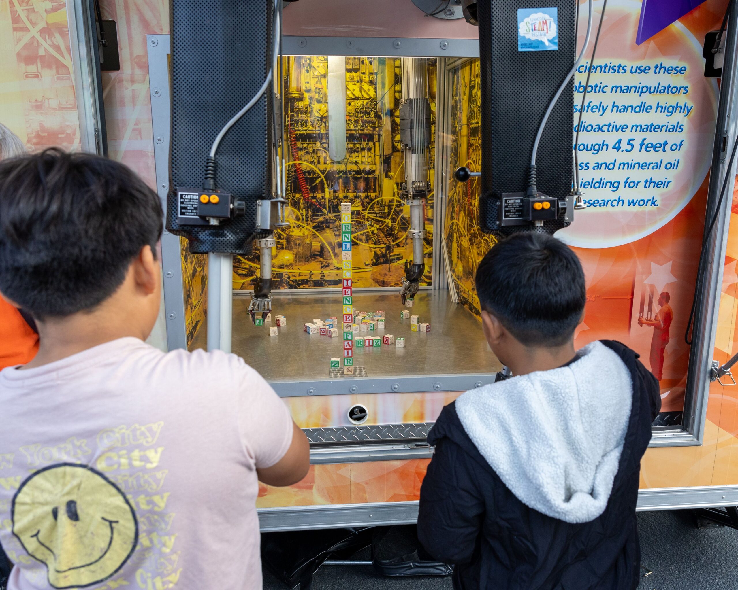 Two students are using the robotic manipulators to move blocks