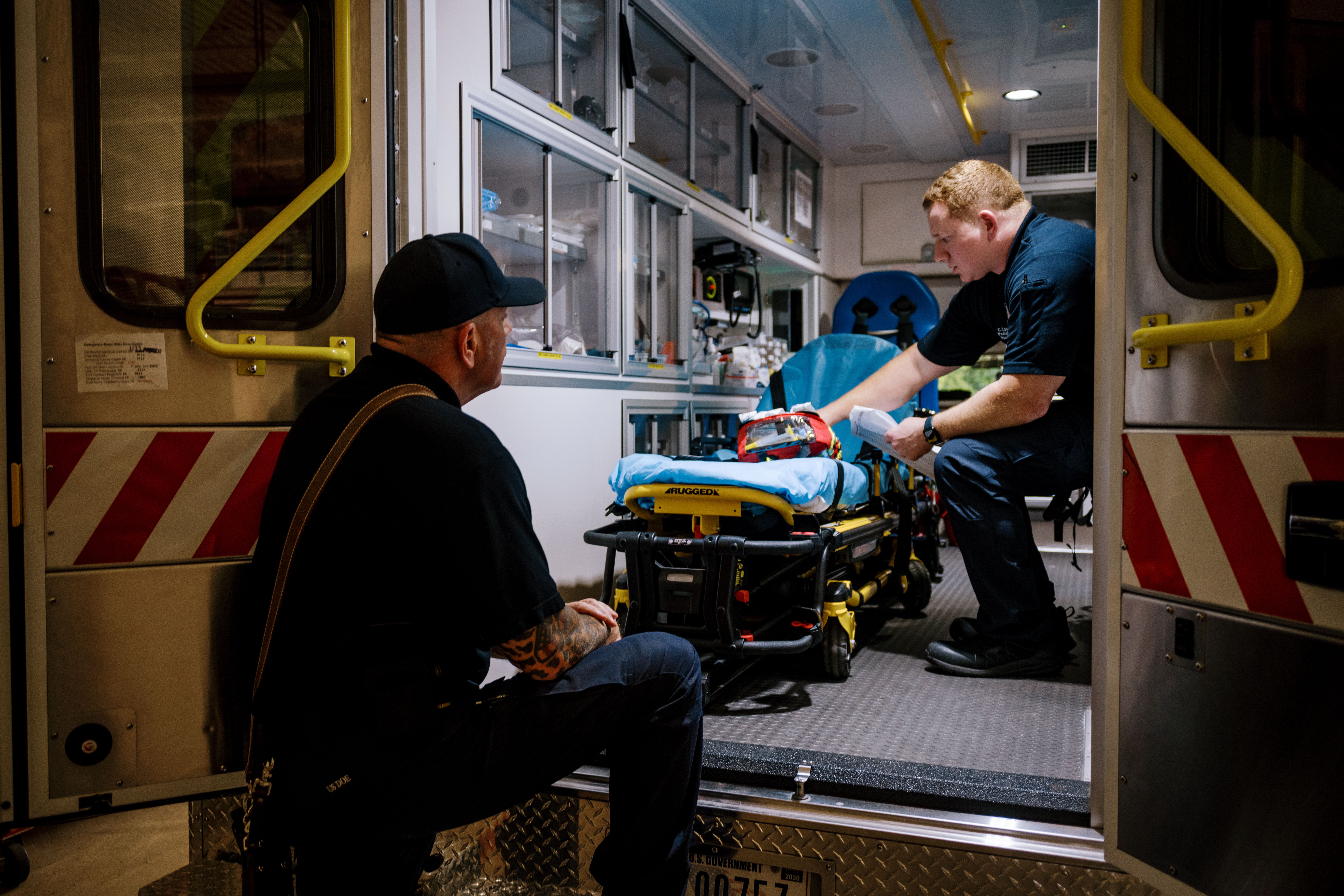 Two firefighters inside an ambulance preparing a stretcher and medical equipment