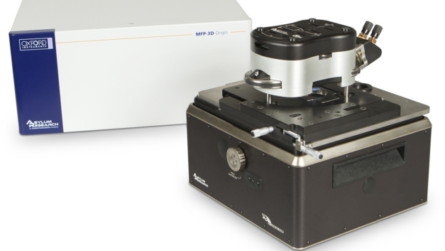 A white enclosed small machine sits next to a black box topped with a metallic cylinder