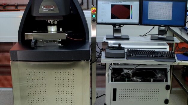 A machine resembling a cast-iron stove sits next to a rolling cart with two monitors