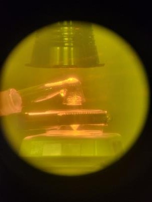Yellow-tinted glovebox view of metal tubes under a heated apparatus.
