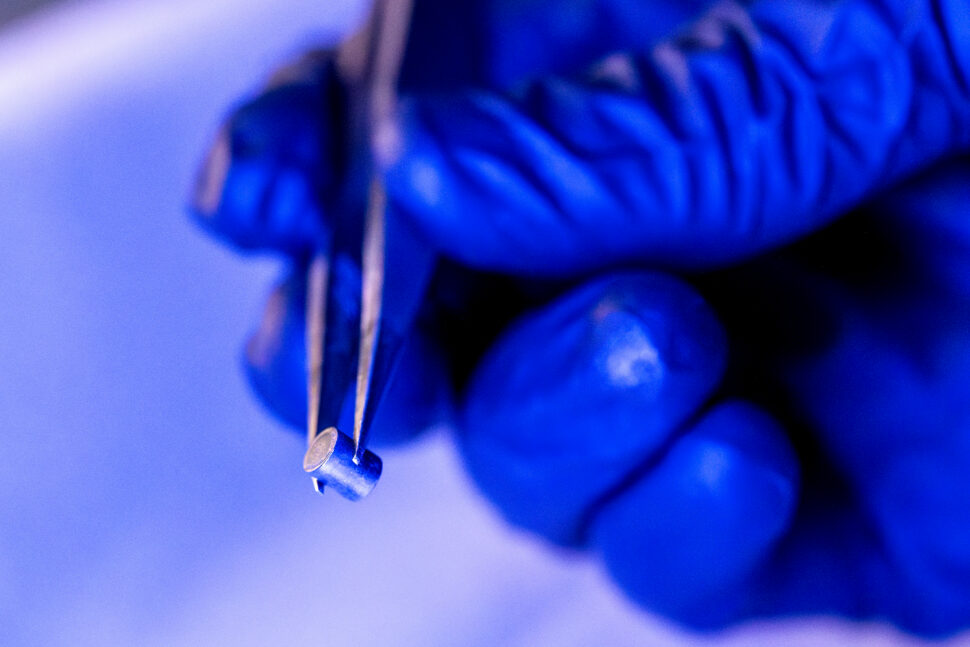 A gloved hand holds a small selenium-74 target capsule with tweezers during radioisotope preparation at Oak Ridge National Laboratory.