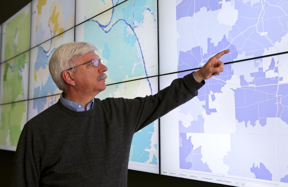 A man points to a highlighted region on a map displayed on a screen.