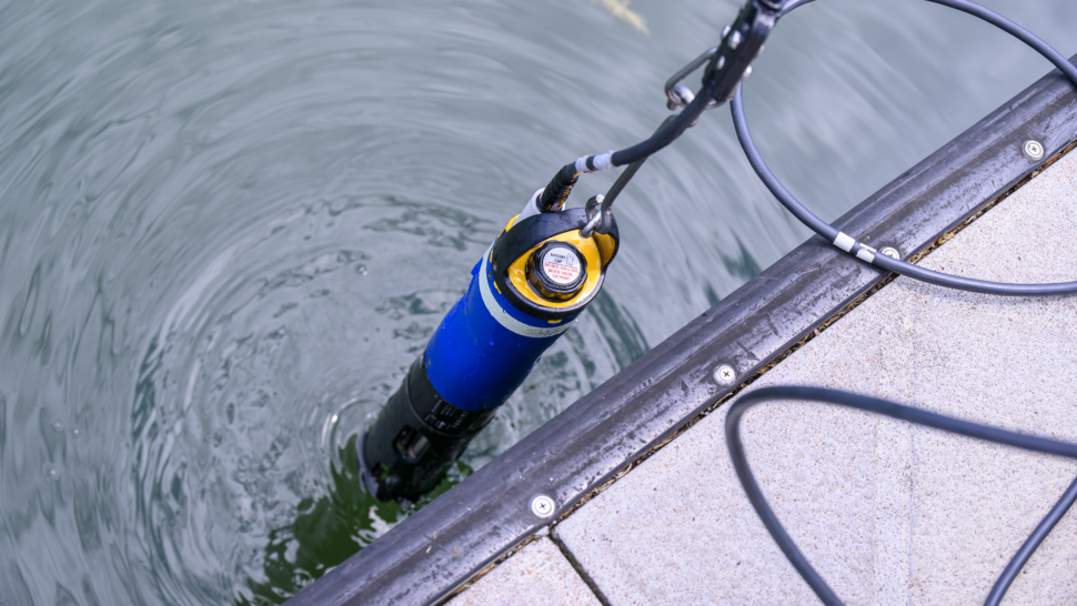 A water-quality monitoring instrument is suspended in the water beside a dock at Melton Hill Dam during the Appalachian Hydropower Workshop. The submerged sensor collects environmental data used to support hydropower research and aquatic monitoring.