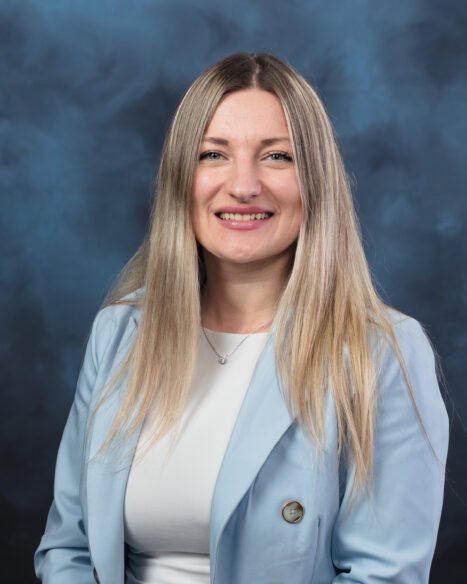 A woman poses for a professional portrait, facing the camera with a background.
