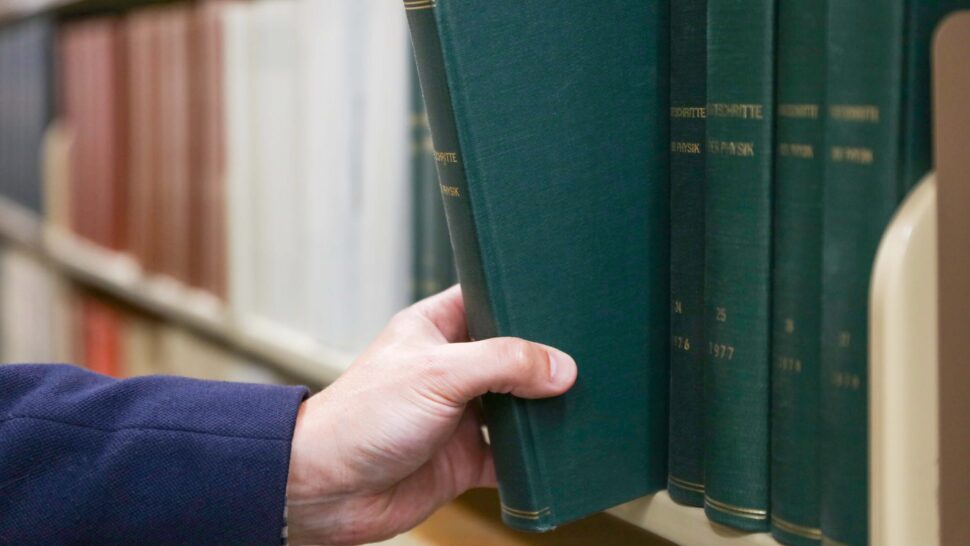 Closeup of hand removing green textbook from library book shelf.