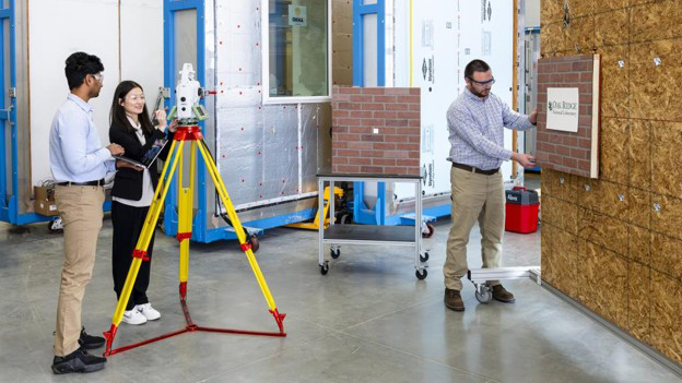 ORNL’s real-time evaluator tool, shown as demonstrated in the laboratory by researchers Nolan Hayes, right, Mengjia Tang, center, and Balaji Selvakumar, left, can guide the positioning of exterior walls.