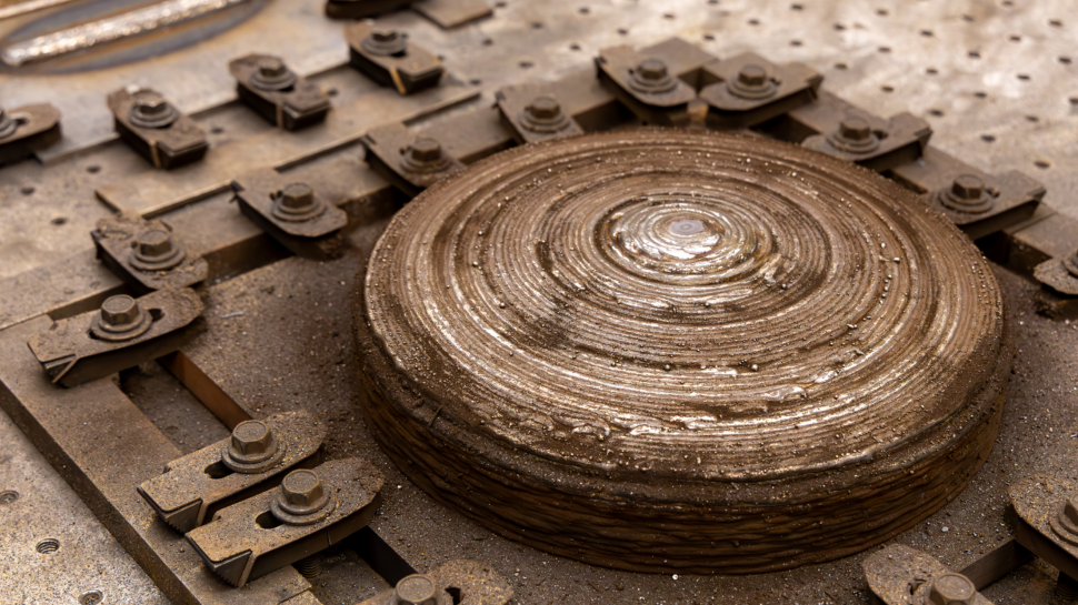 Close-up view of a wire-arc additively manufactured metal dome showing layered deposition patterns and metallic surface texture.
