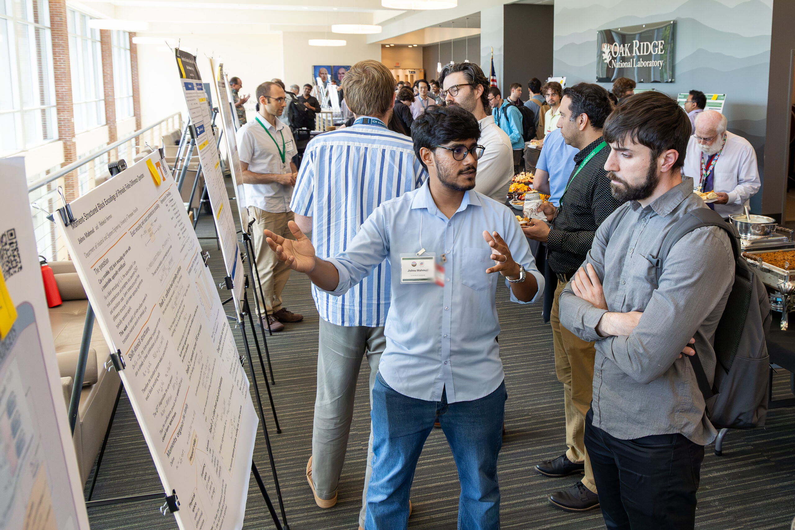 Jishnu Mahmud explains his research poster to an attendee during the poster session at the 2026 Quantum Computing User Forum while other participants network and view research displays in the background.