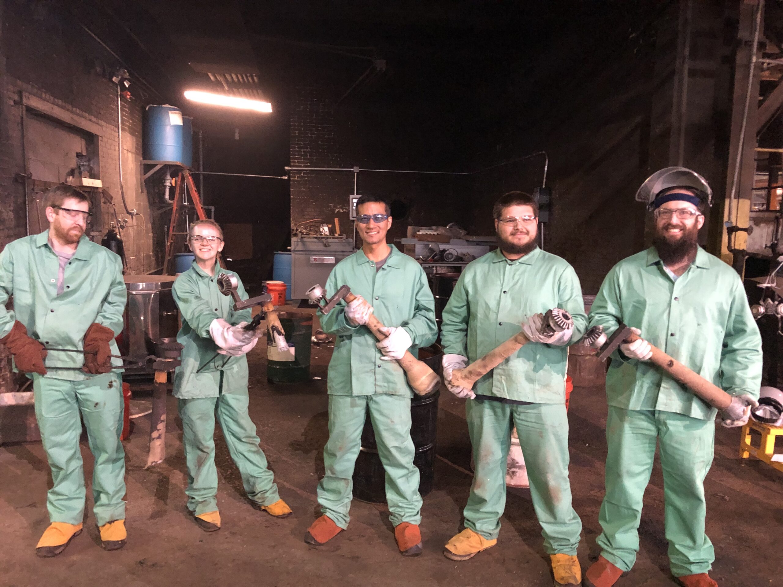 Group of smiling individuals dressed in protective gear in a factory. Image via Skuld
