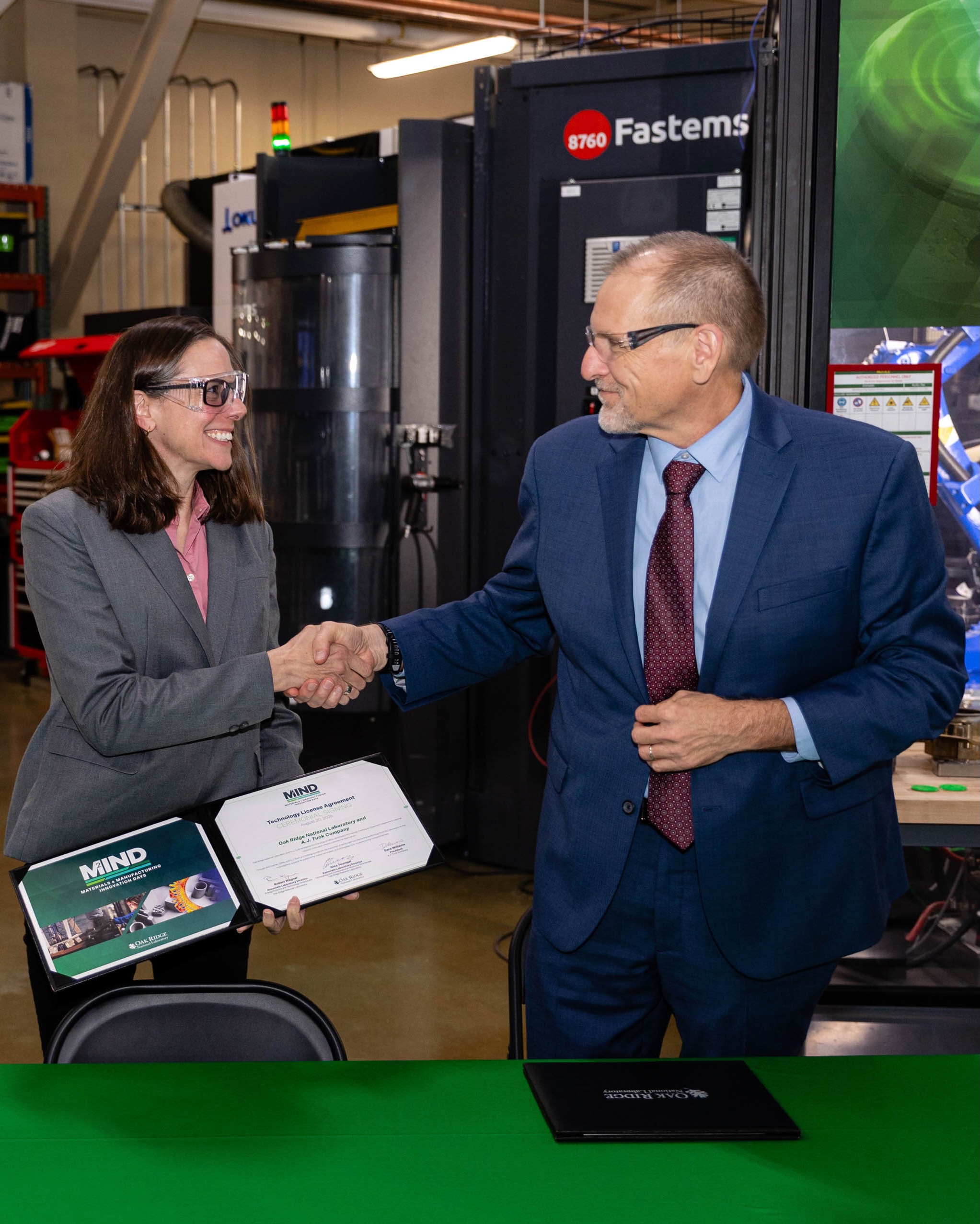 Dara Williams, of A.J. Tuck, and Robert Wagner, ORNL associate laboratory director for Energy Science and Technology, shake hands in a licensing ceremony during ORNL Materials and Manufacturing Innovation Days at the Manufacturing Demonstration Facility.
