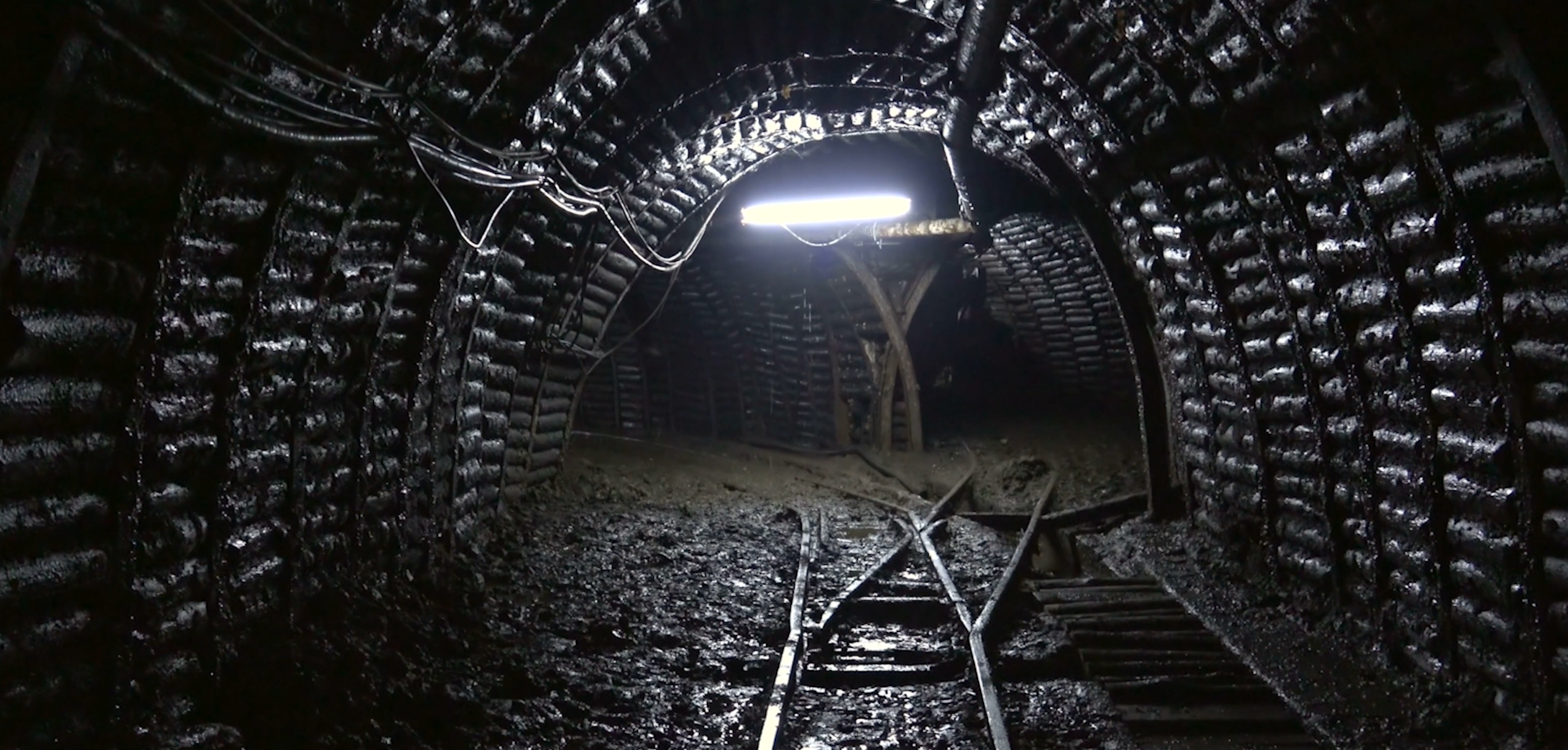 An image of a mine shaft in black and grey, lit by a single light in the middle