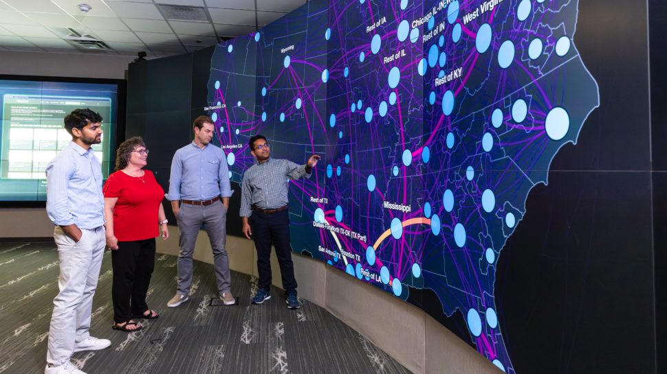 From left, Pankaj Dahal, Stacy Davis, Majbah Uddin and David McCollum pose together in front of modeling and analytics displayed on the EVEREST visualization system.