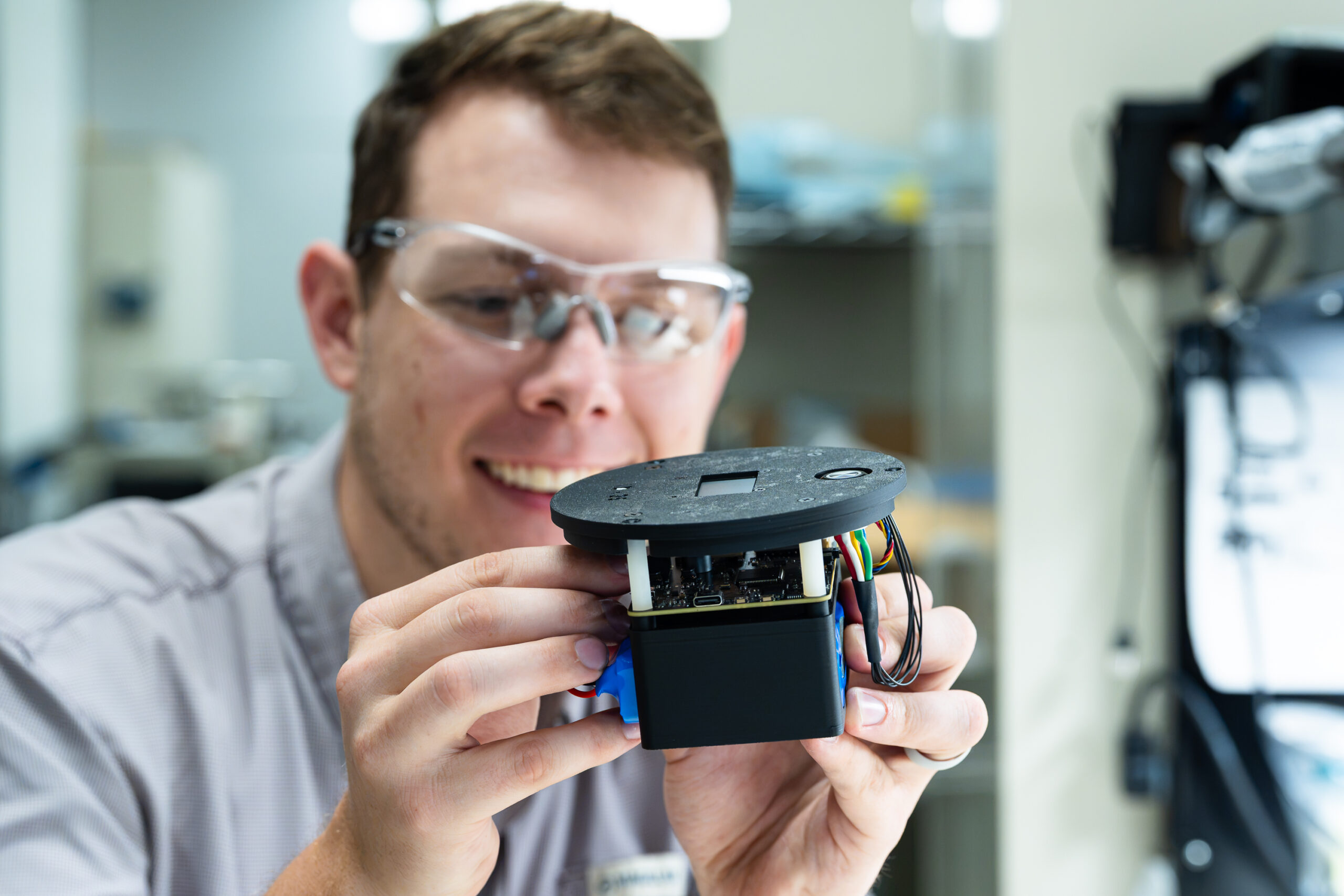 Researcher examines a compact monitoring device in a laboratory.