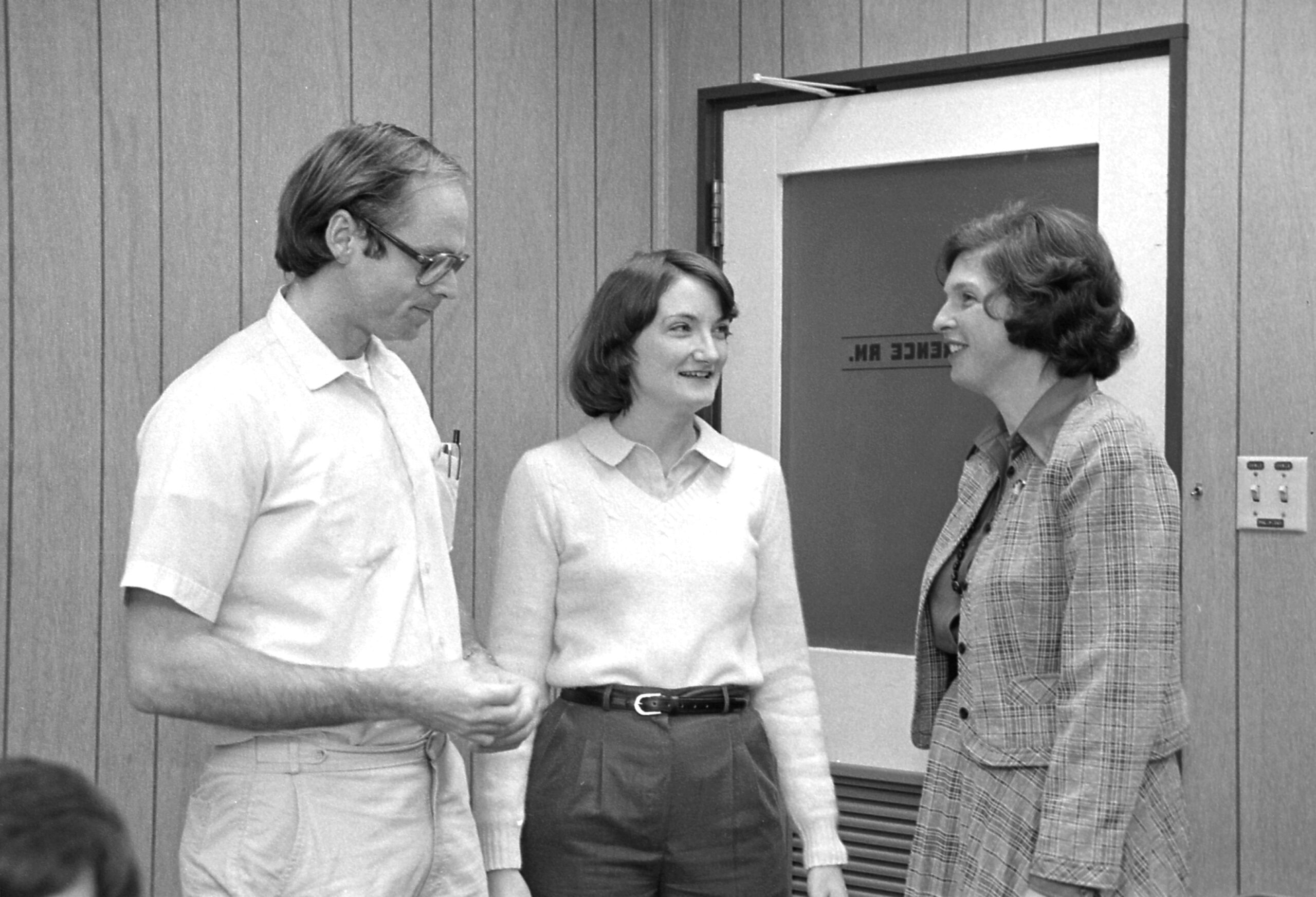 Two women and a man talk in a black-and-white photo