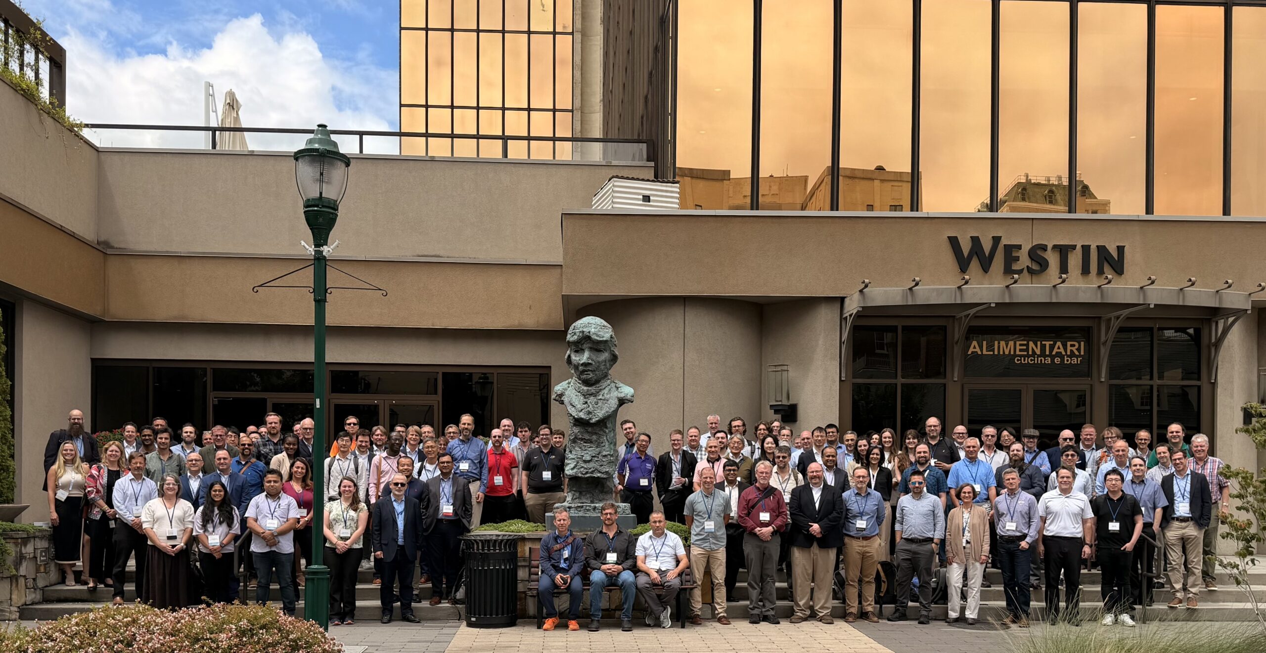Conference attendees pose for a group photo outside a hotel.