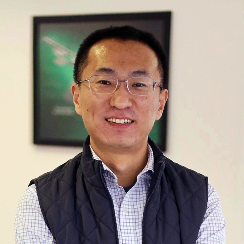 A man in a vest stands in front of a green poster